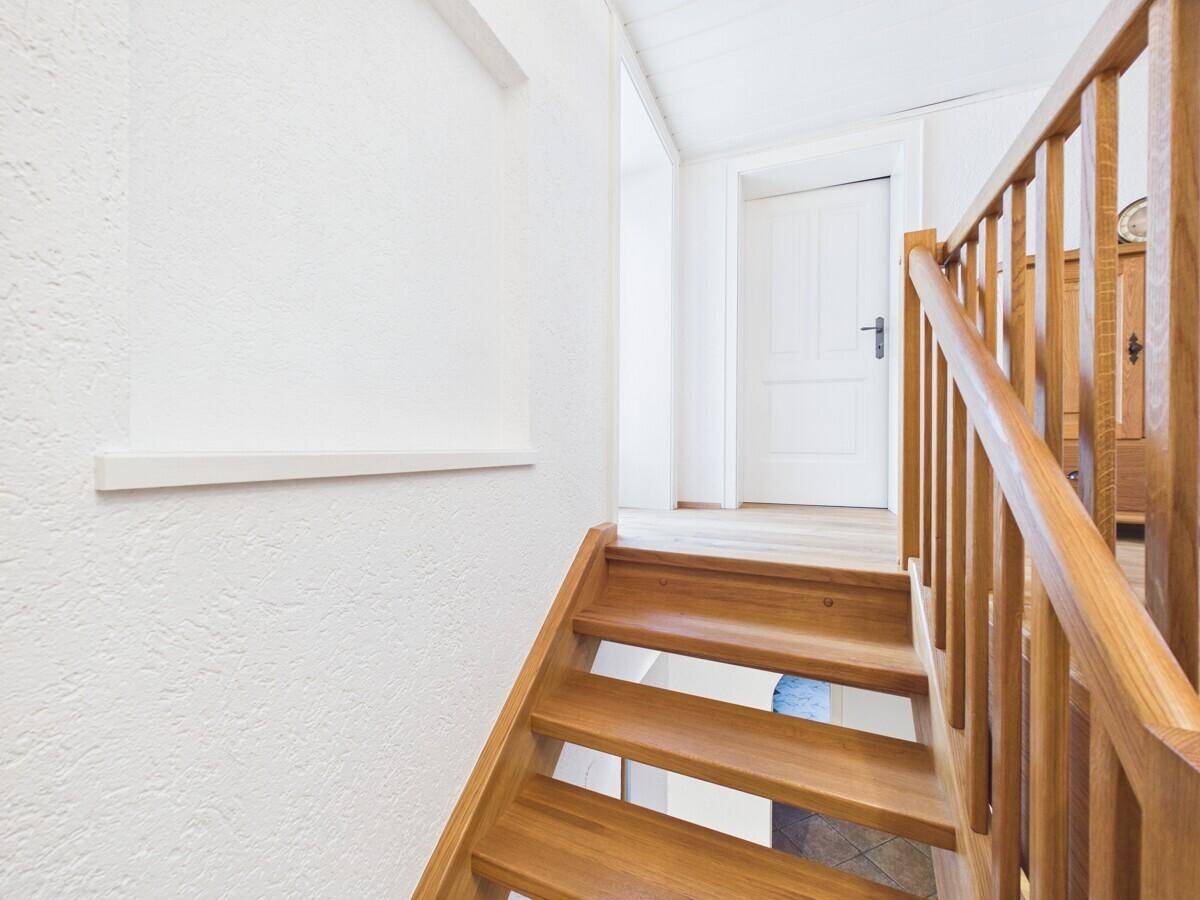 Helle Holztreppe führt in den oberen Bereich, mit weiß gestrichenen Wänden und Holzboden.
