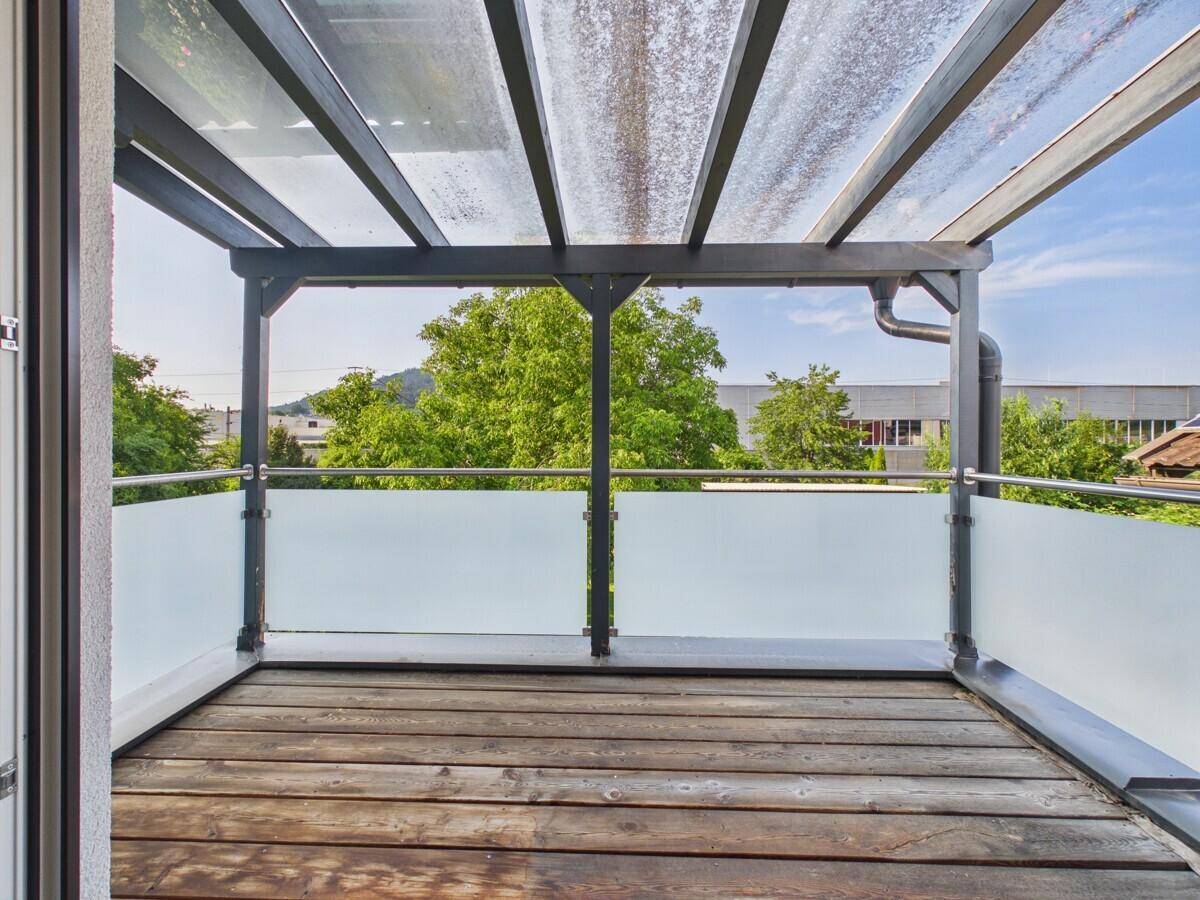 Überdachter Balkon mit Holzboden und moderner Glasbrüstung, bietet einen Ausblick ins Grüne.