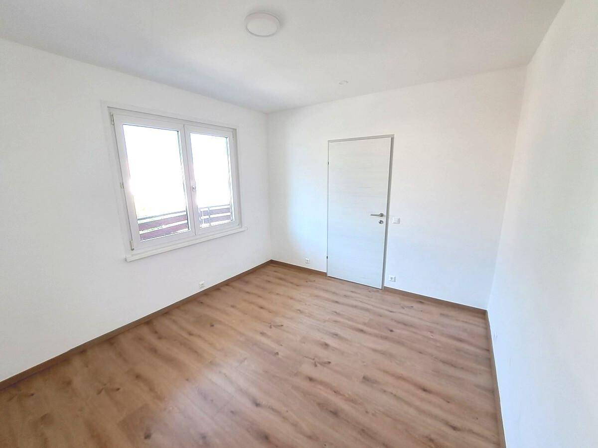 Schlafzimmer mit Laminatboden, weiß gestrichenen Wänden und Fenster mit Blick auf einen Balkon.