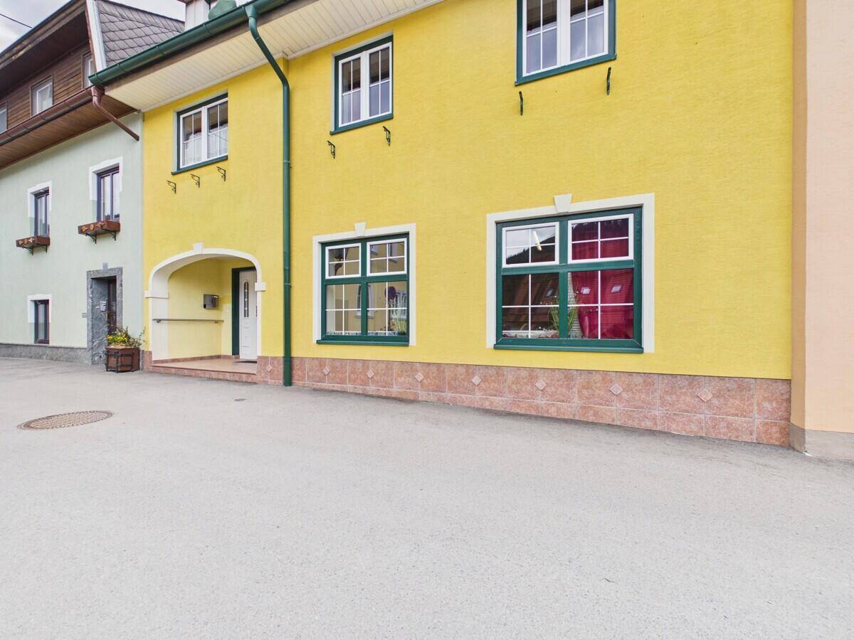 Gelbe Hausfassade mit grünen Fensterrahmen und traditioneller Architektur in ländlicher Umgebung.