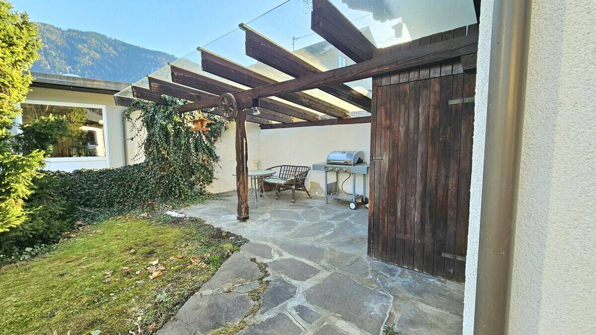 Überdachte Terrasse mit Grillbereich, Steinfliesen und Gartenblick.