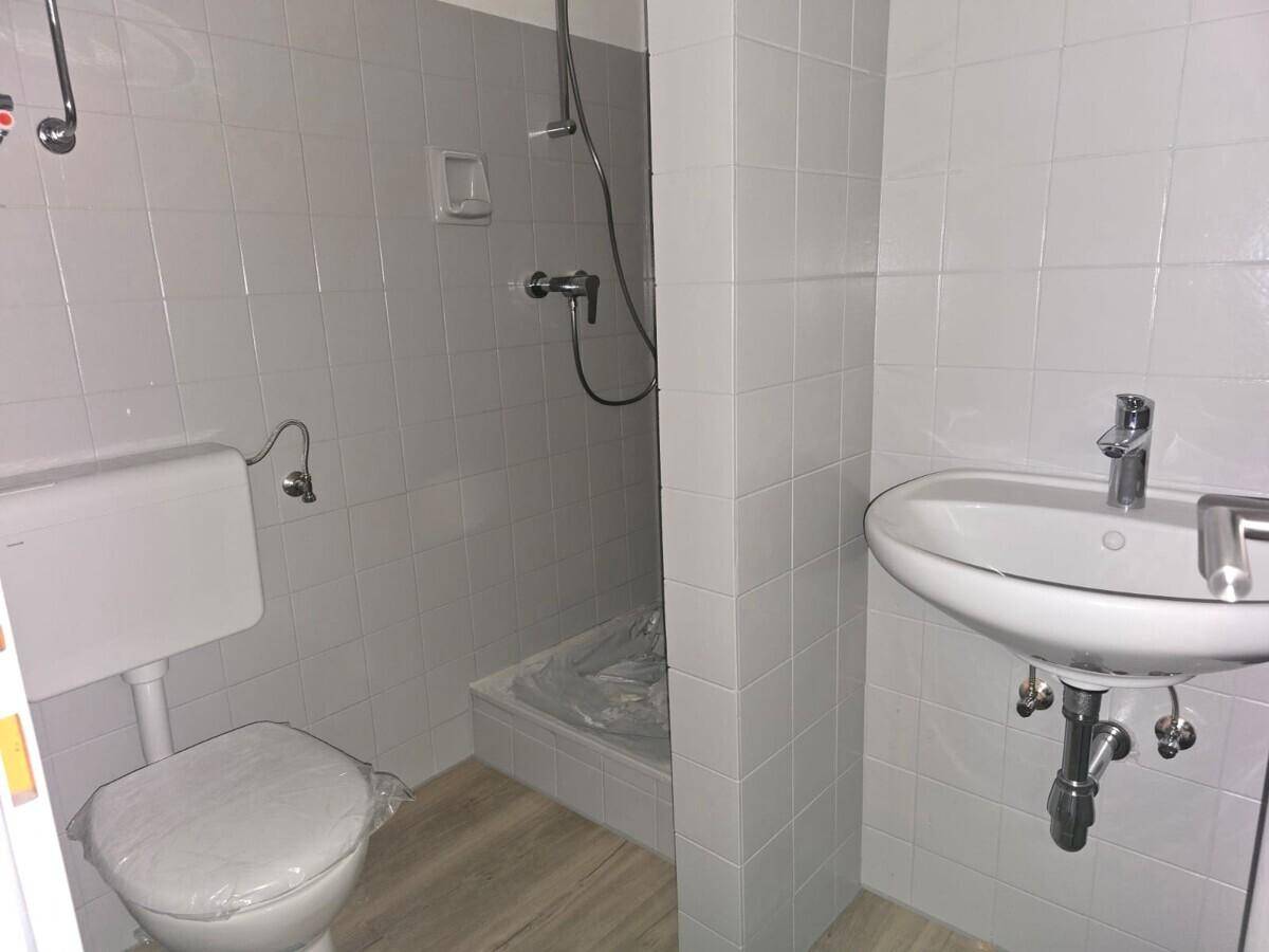 Funktionales Badezimmer mit hellgrauen Fliesen, einer Duschkabine und einem Waschbecken.