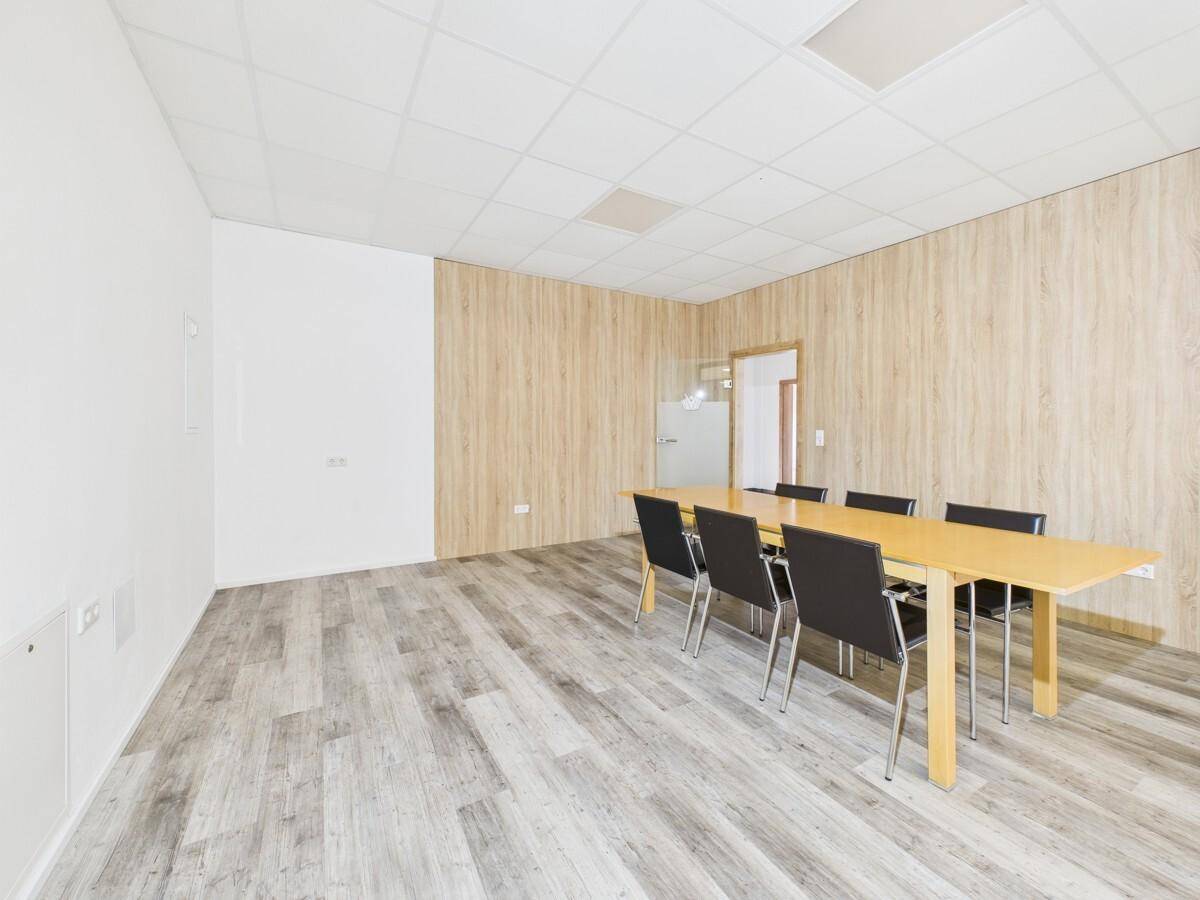 Konferenzraum mit Holztisch und Stühlen, Laminatboden und Holzwandverkleidung.