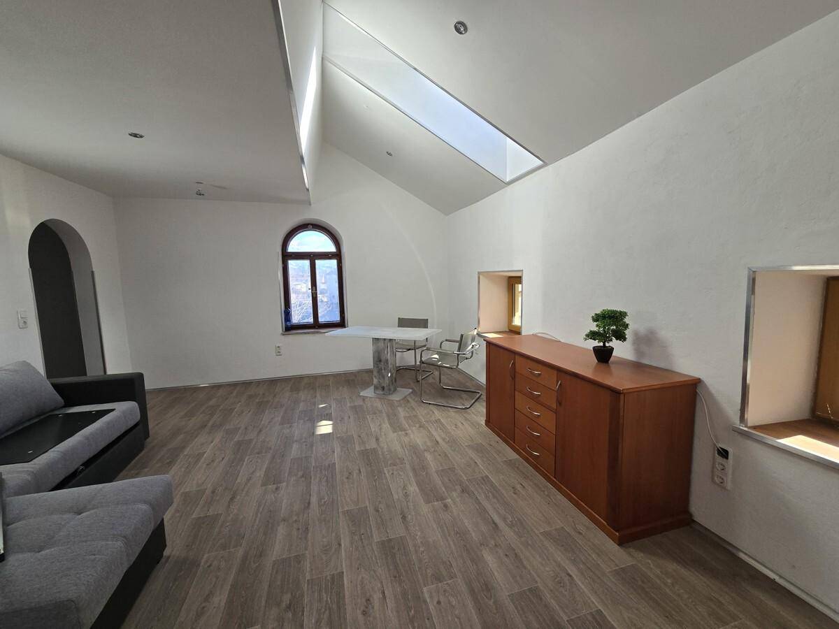 Heller Wohn-Essbereich mit Holzboden, Dachfenster und einem Bogenzugang zu weiteren Räumen.