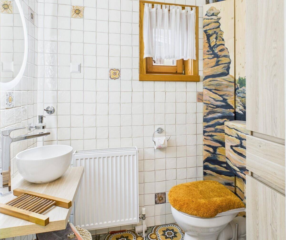 Badezimmer mit WC, weiß gefliesten Wänden und einem kleinen Fenster für Tageslicht.