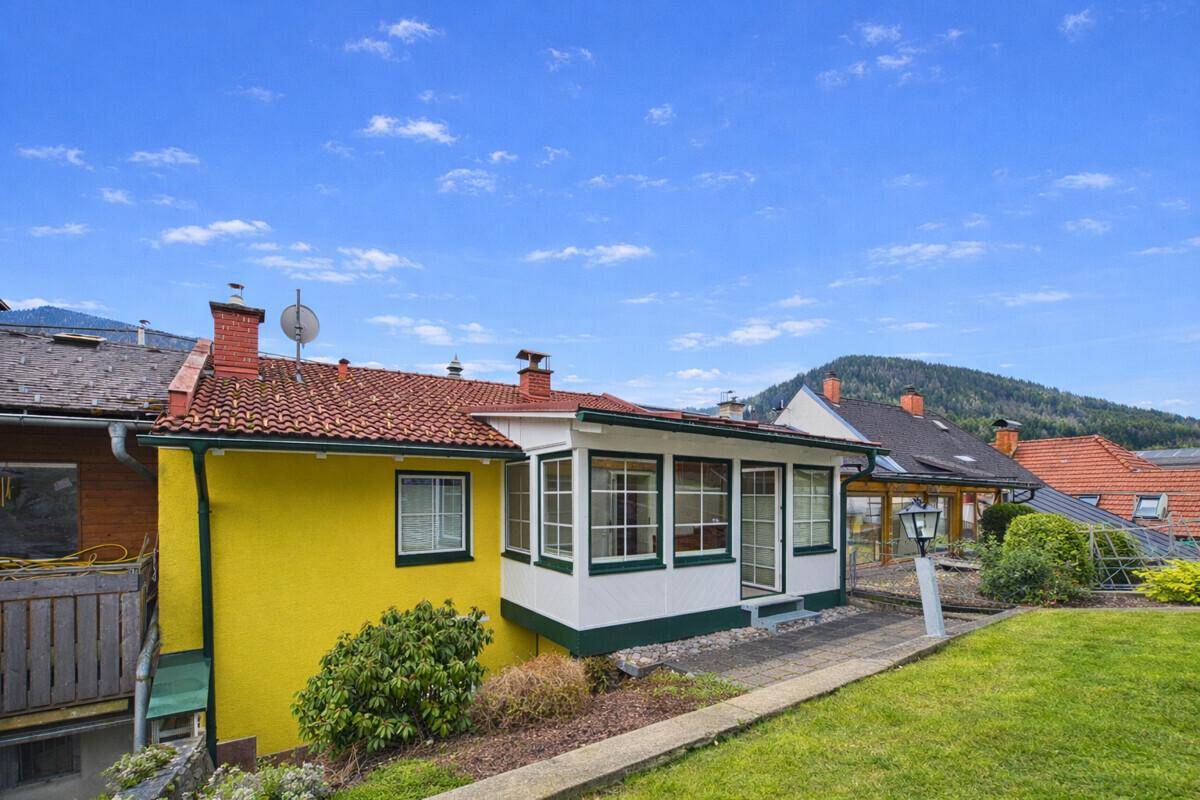 Rückseite des Hauses mit Wintergarten, gepflegtem Rasen und Blick auf die umliegende Landschaft.
