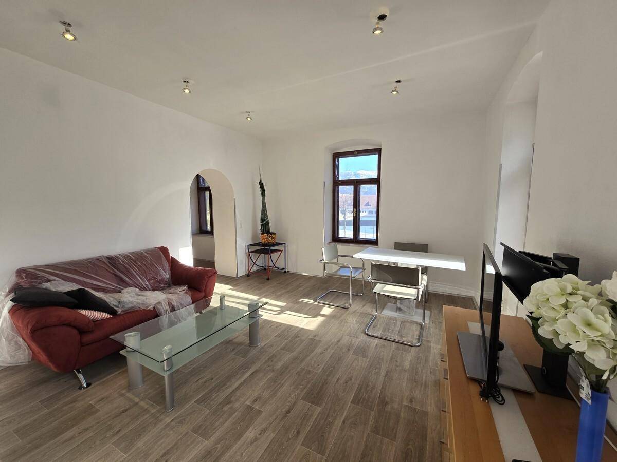 Helles Wohnzimmer mit Holzboden, rotem Sofa und einem Esstisch, ideal für gesellige Abende.