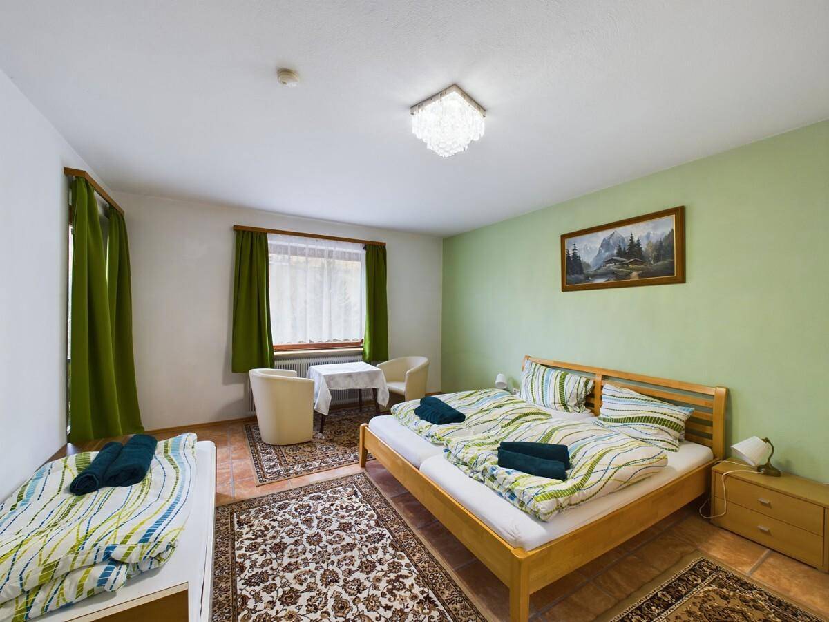 Helles Schlafzimmer mit Doppelbett, grün gestrichenen Wänden und Teppichen auf Fliesenboden.