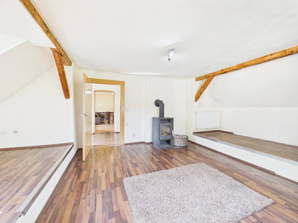 Gemütlicher Dachbodenraum mit sichtbaren Holzbalken, einem Holzofen und einer erhöhten Plattform.