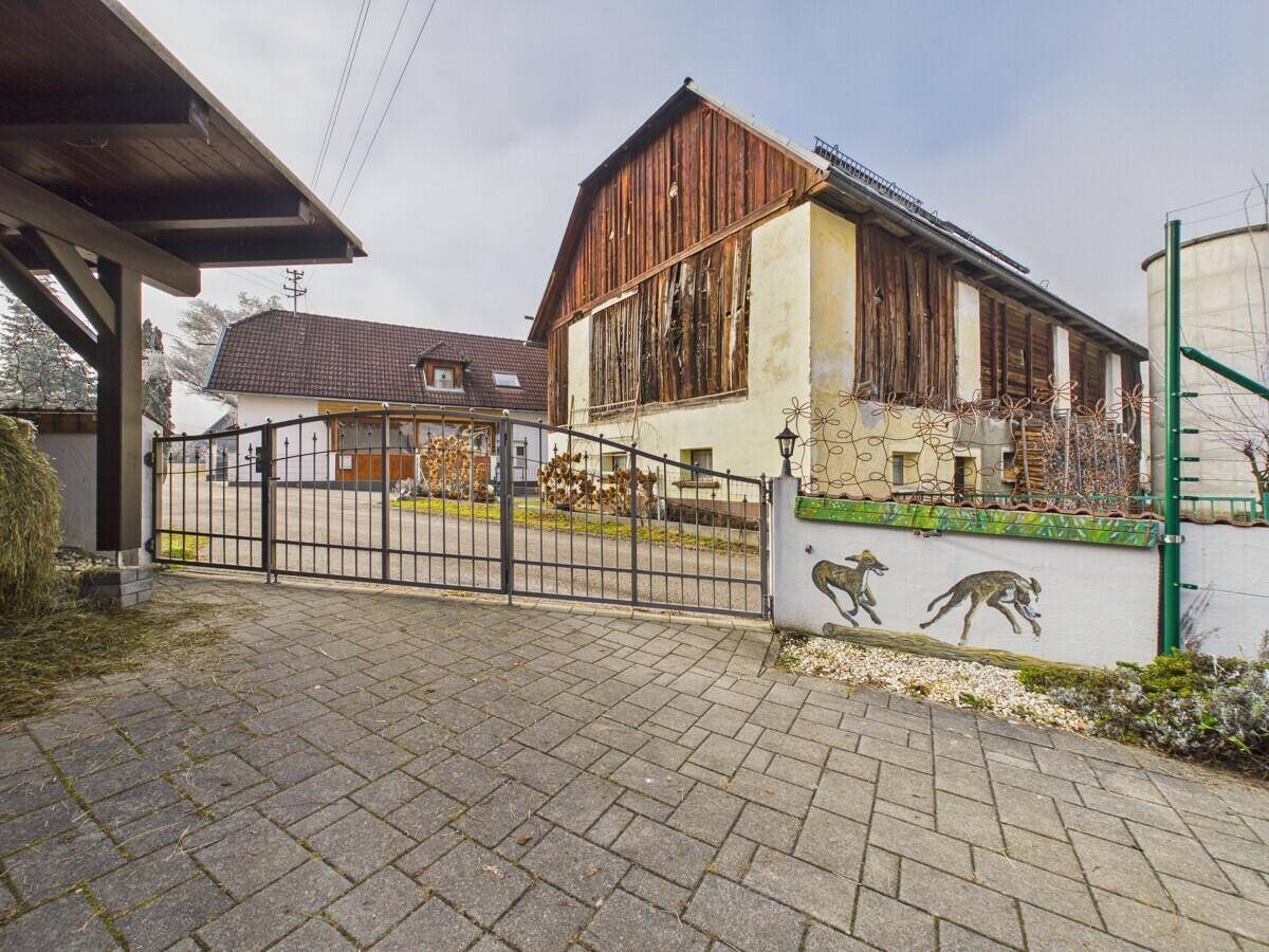 Eingangsbereich eines ländlichen Anwesens mit schmiedeeisernem Tor und mehreren Gebäuden.