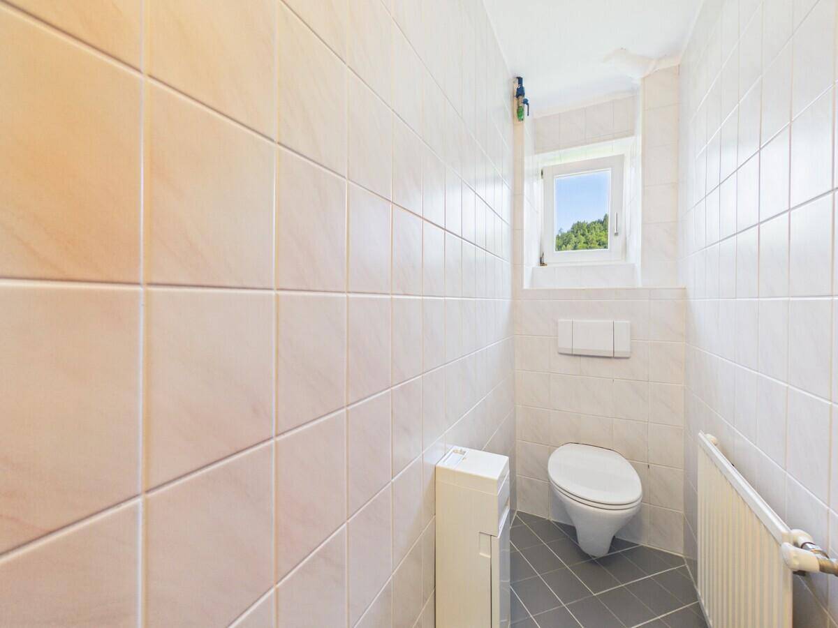Kleines Gäste-WC mit Wand-WC, Fliesenboden und Fenster für natürliche Belüftung.