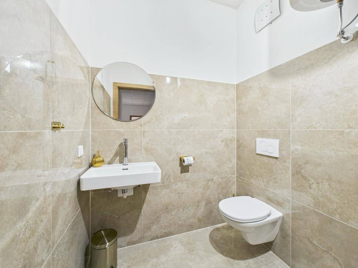Modernes Gäste-WC mit beigefarbenen Fliesen, wandhängendem WC und kleinem Waschbecken.