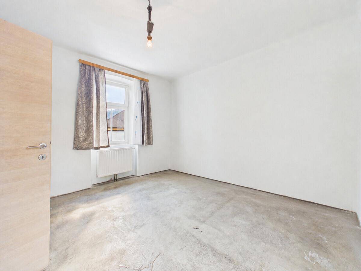 Unfertiger Raum mit Betonboden, einem Fenster und einer hellen Holztür, wartet auf den Ausbau.