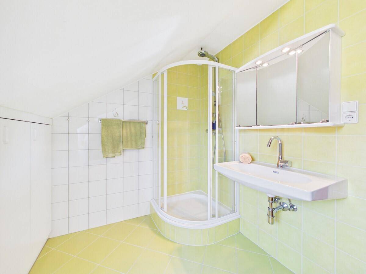 Badezimmer im Dachgeschoss mit Duschkabine, Waschbecken und hellgrünen Fliesen.