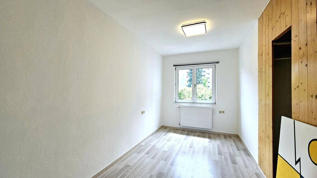 Helles Schlafzimmer mit Laminatboden, Fenster und Holzwand mit integriertem Schrank.