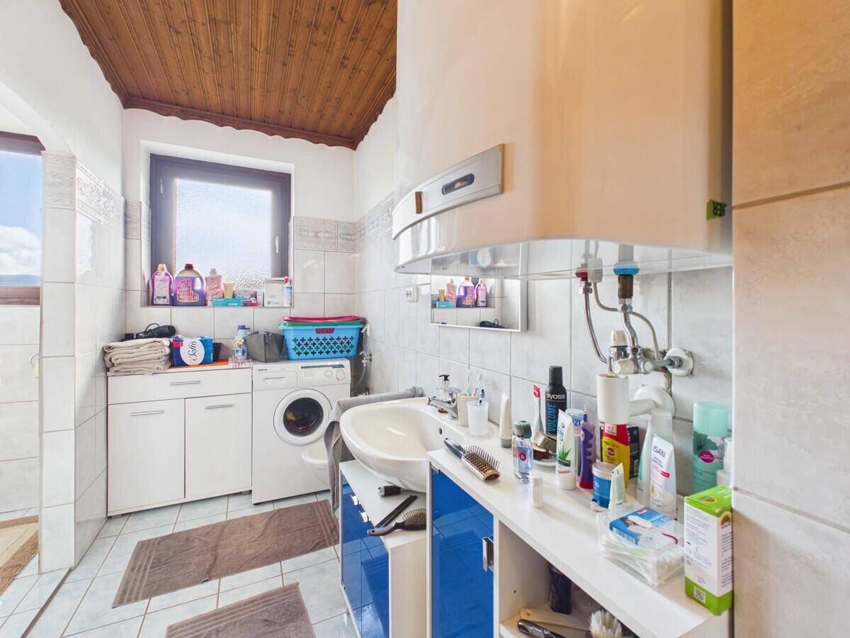 Badezimmer mit Waschmaschine, Waschbecken und Fenster, gefliest in hellen Tönen.