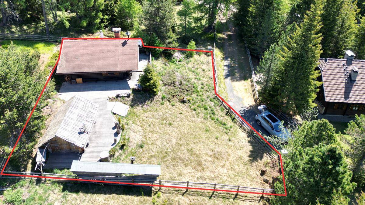 Luftaufnahme eines rustikalen Anwesens mit mehreren Holzhütten und umzäuntem Grundstück in grüner Umgebung.