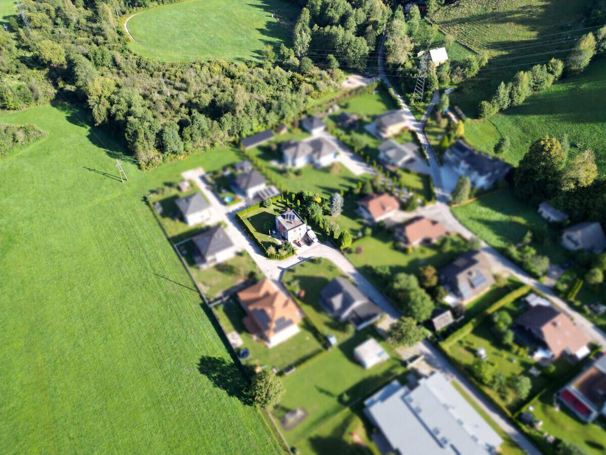 Weitläufige Luftaufnahme der Wohnsiedlung, umgeben von Feldern, Wäldern und Bergen.