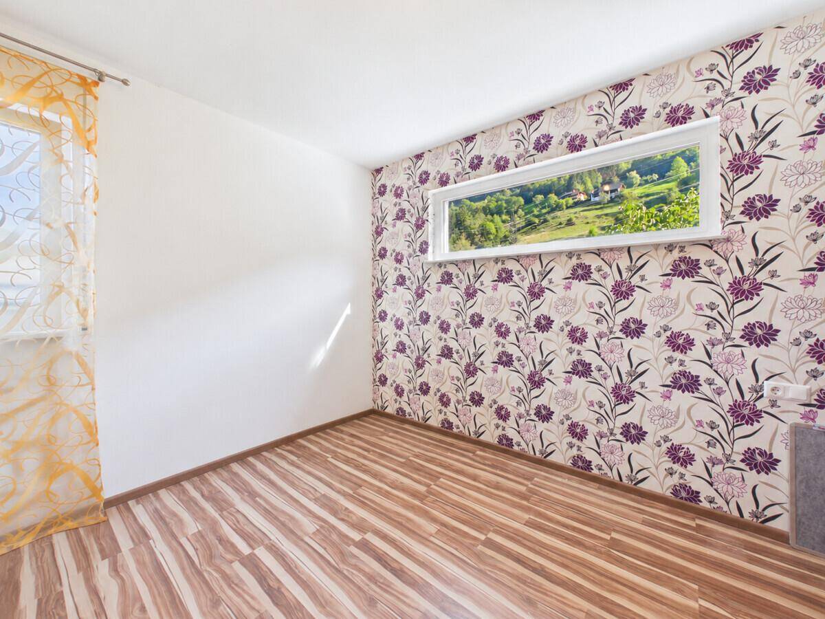 Geräumiges Zimmer mit floraler Mustertapete, Laminatboden und weitem Ausblick.