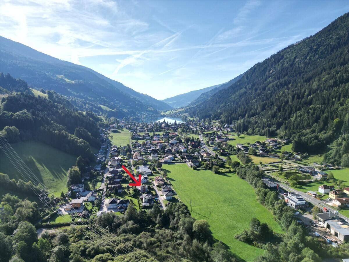 Weitläufige Luftaufnahme eines Tals mit See, umgeben von Bergen und einer Siedlung.