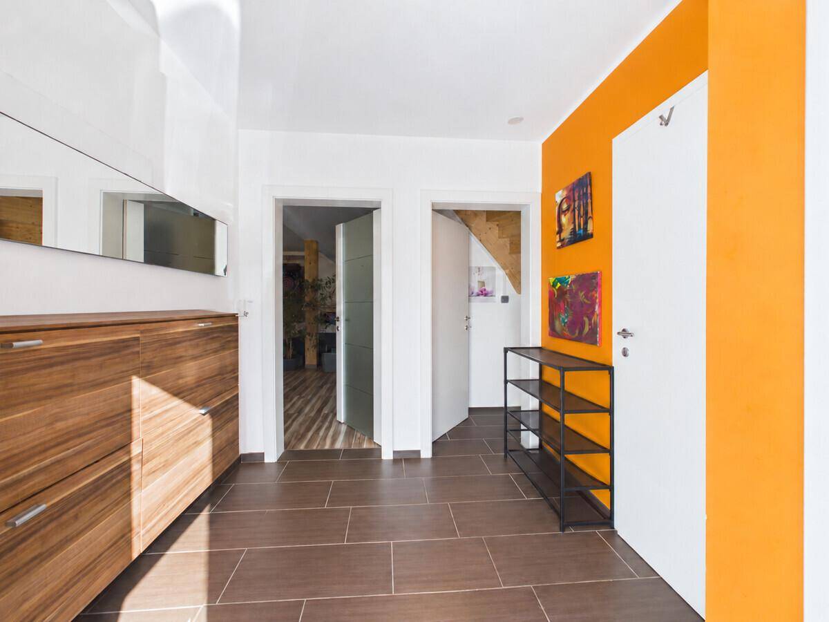 Heller Flur mit dunklem Fliesenboden, Holzschuhschrank und einer farbigen Akzentwand.