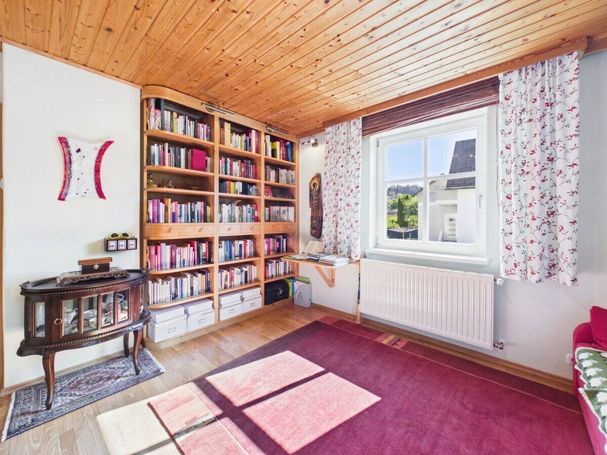 Gemütliches Arbeitszimmer mit Holzbalkendecke, großem Bücherregal und Blick ins Grüne.
