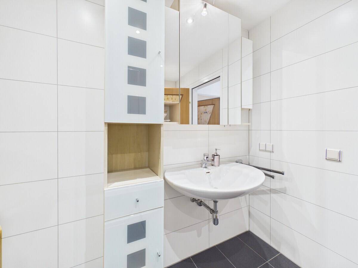 Helles Badezimmer mit Waschbecken, Spiegelschrank und weißen Wandfliesen.