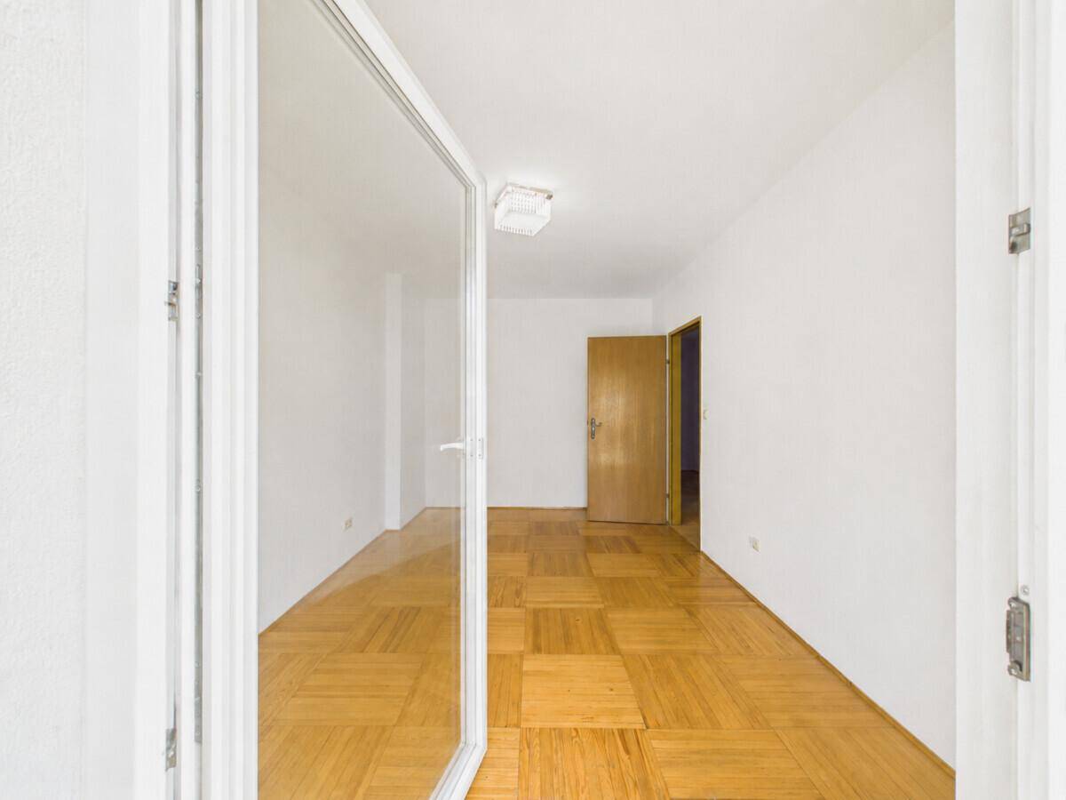 Heller Raum mit Parkettboden und großer Glastür, die ins Freie führt.