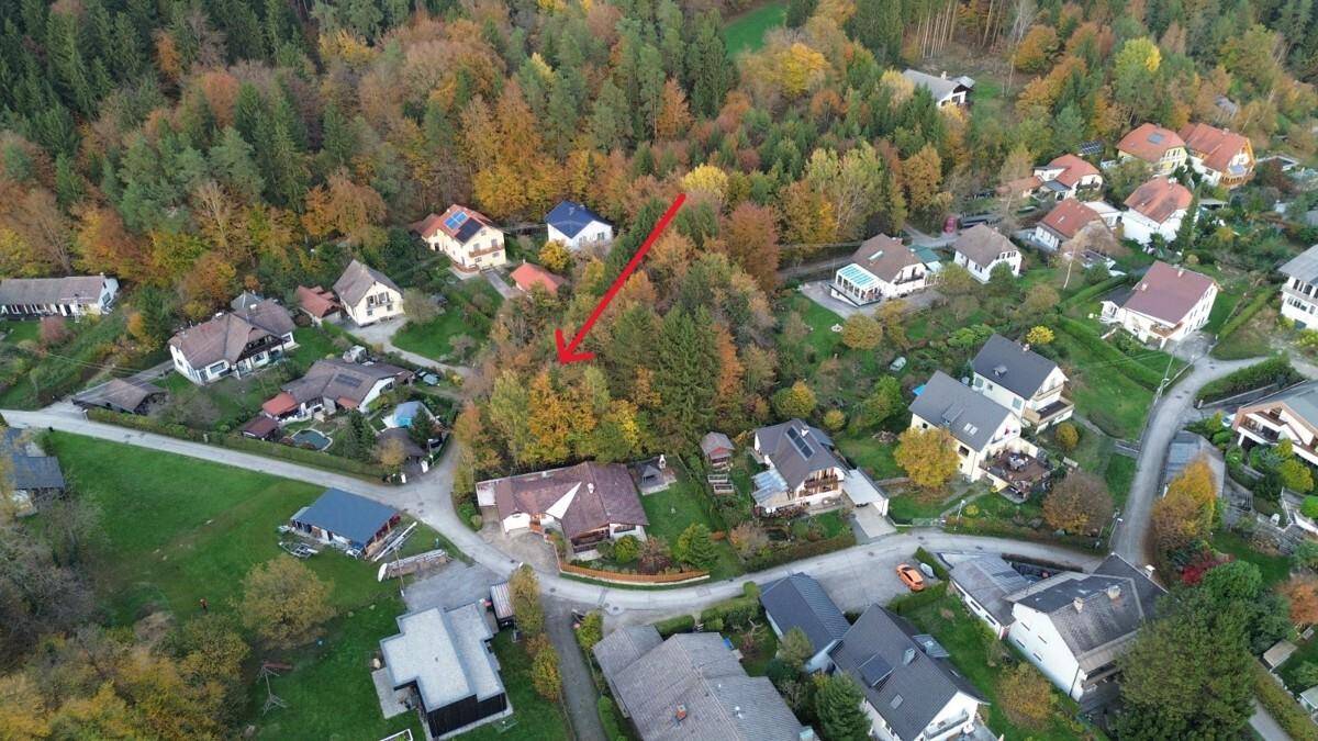 Herbstliche Luftaufnahme eines Wohngebiets mit bunten Bäumen und einem roten Pfeil, der auf das Grundstück weist.