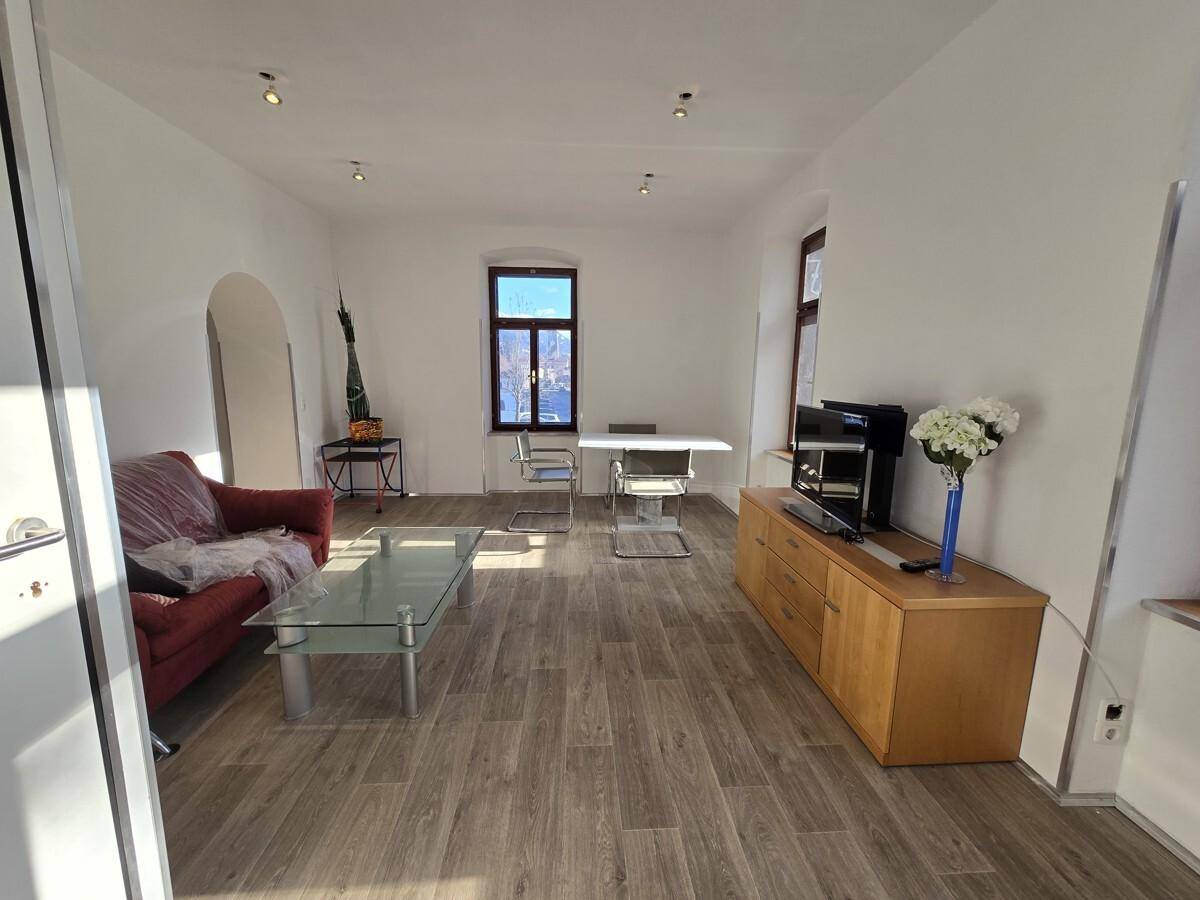 Helles Wohnzimmer mit Holzboden, rotem Sofa und einem Esstisch, ideal für gesellige Abende.