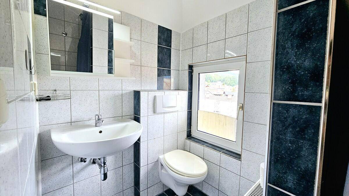 Gefliestes Badezimmer mit Waschbecken, Toilette, Spiegelschrank und Fenster.