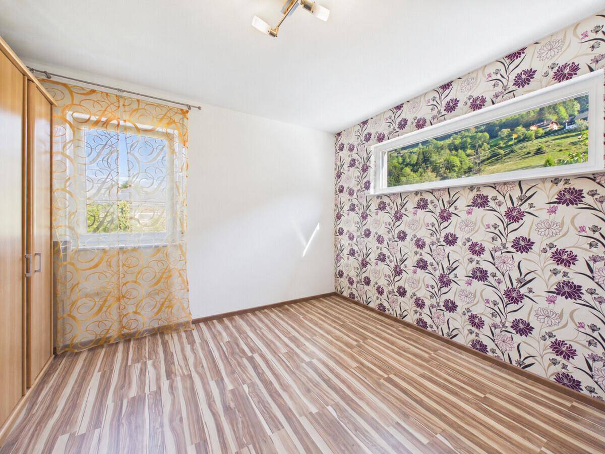 Helles Zimmer mit floraler Tapete, Laminatboden und Blick ins Grüne.