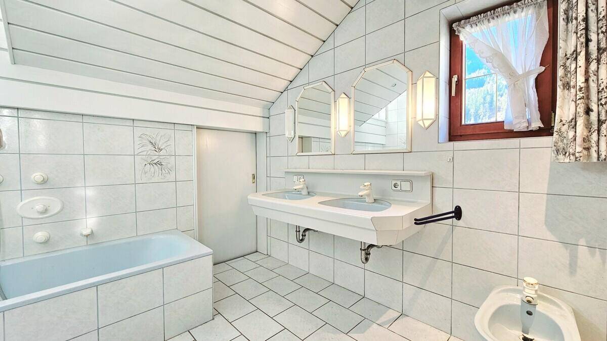Helles Badezimmer mit Doppelwaschbecken, Badewanne und Dachschrägen.