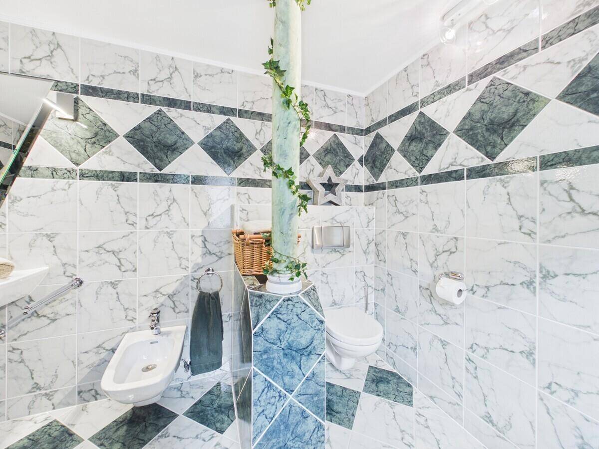 Badezimmer mit Bidet, wandhängendem WC und dekorativen grün-weißen Marmorfliesen.