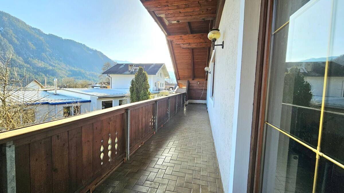 Langer Holzbalkon mit Fliesenboden und sonnigem Blick auf die Umgebung.