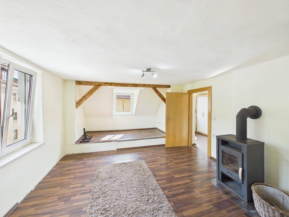 Geräumiger Dachbodenraum mit Holzofen, sichtbaren Holzbalken und Laminatboden, bietet vielseitige Nutzungsmöglichkeiten.
