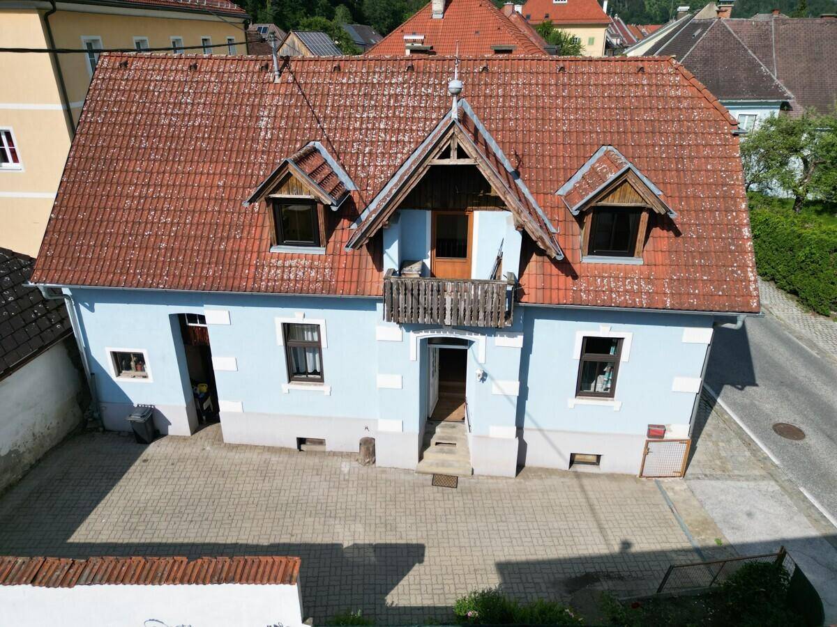 Vorderansicht des Hauses mit blauer Fassade, rotem Ziegeldach und einem kleinen Holzbalkon.