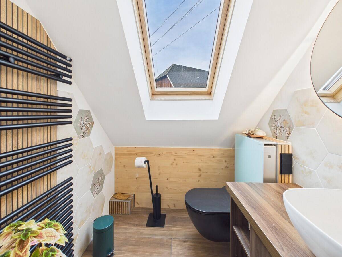 Modernes Badezimmer im Dachgeschoss mit WC, Waschbecken und einem großen Dachfenster.