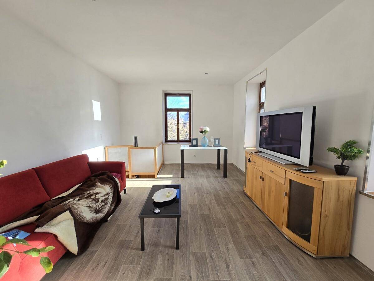 Helles Wohnzimmer mit Holzboden, rotem Sofa und Blick auf die Landschaft durch das Fenster.