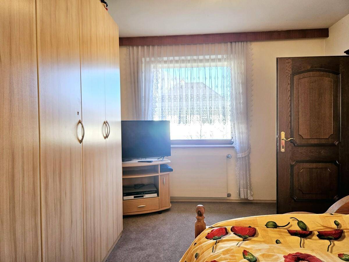 Schlafzimmer mit Teppichboden, Kleiderschrank und Fenster mit Vorhängen.