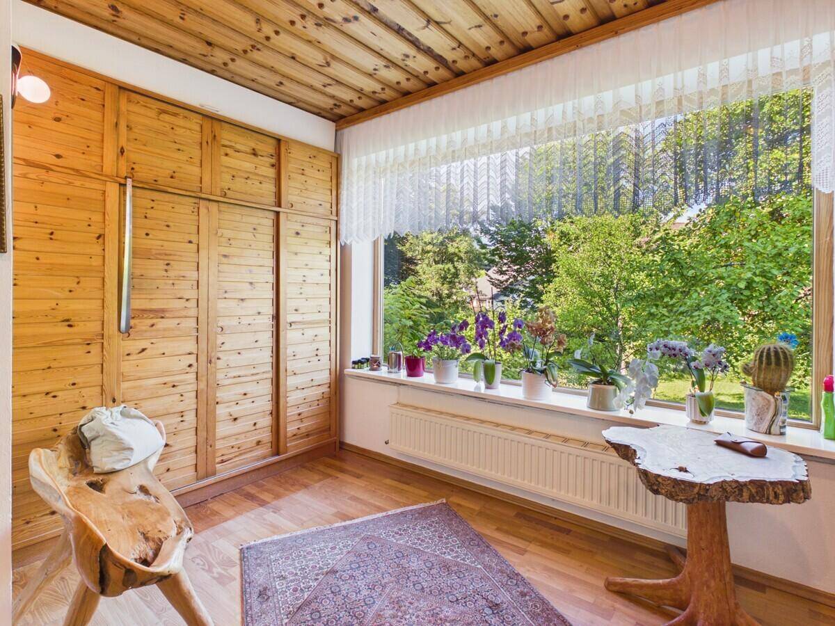 Gemütliches Zimmer mit Holzvertäfelung, Parkettboden und großem Fenster mit Blick ins Grüne.