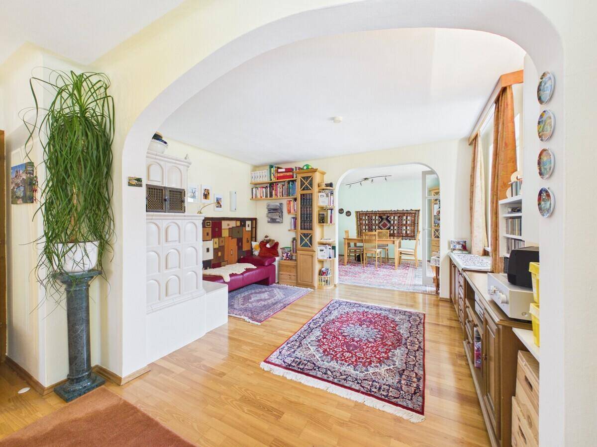 Geräumiges Wohnzimmer mit Holzboden, Kachelofen und offenem Übergang zum Essbereich.