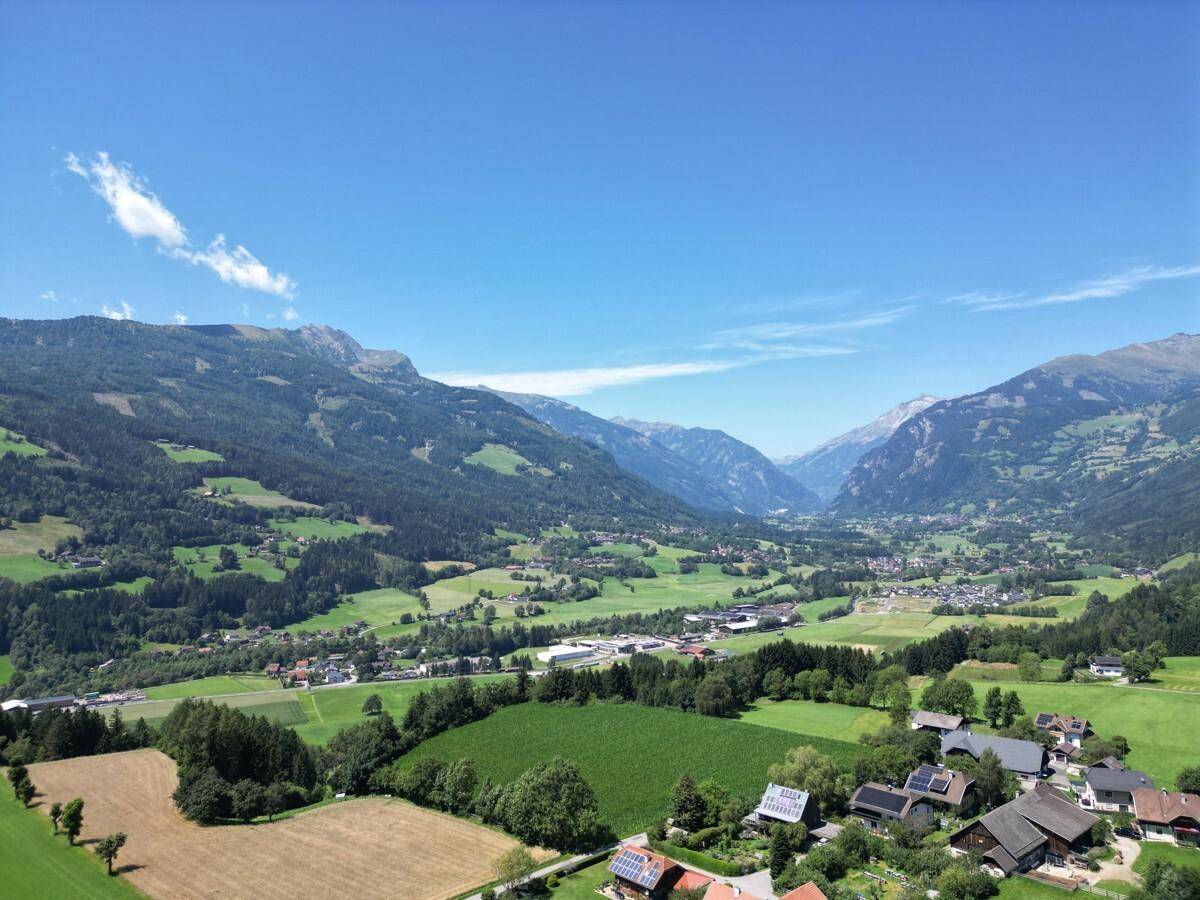 Panoramische Luftaufnahme eines weiten Tals mit Fluss, Dörfern, grünen Feldern und hohen Bergen unter klarem Himmel.