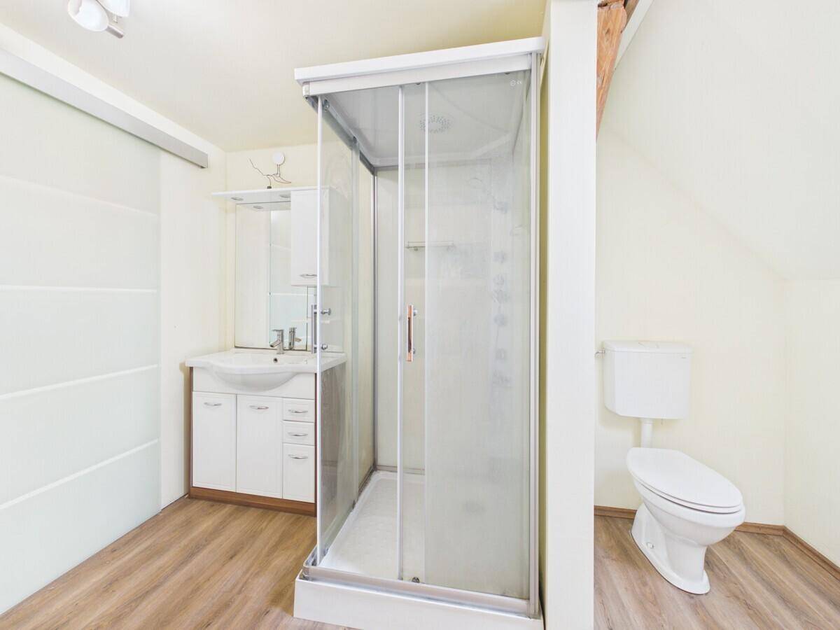 Badezimmer im Dachgeschoss mit Duschkabine, Waschbeckenunterschrank und Toilette, unter sichtbaren Holzbalken.