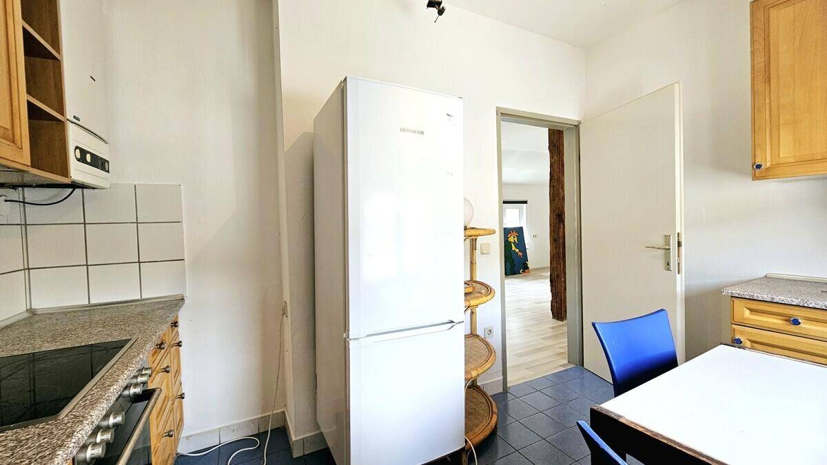 Praktische Küche mit Kühlschrank und Durchgang zum hellen Wohnbereich.