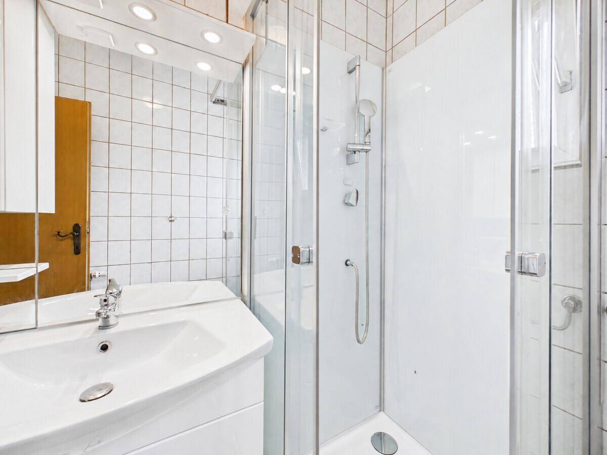 Modernes Badezimmer mit weißen Fliesen, Waschbecken und Duschkabine.