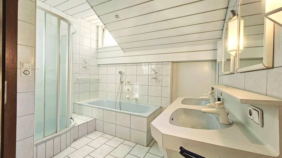 Badezimmer mit Dusche, Badewanne, Doppelwaschbecken und Dachschräge.