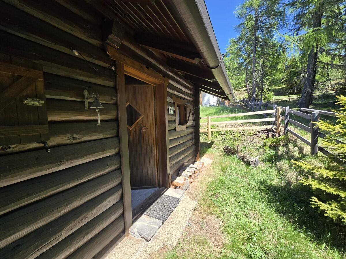 Rustikaler Eingang einer Holzhütte mit Holztür, Fußmatte und einer kleinen Glocke.