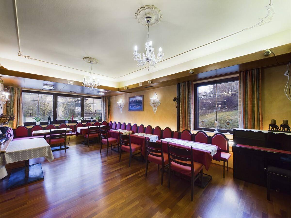 Geräumiger Speisesaal mit Holzboden, eleganten Kronleuchtern und Blick ins Grüne.