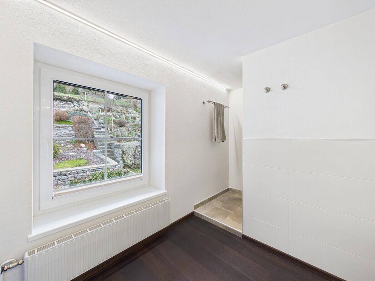 Helles Badezimmer mit Fenster, dunklem Holzboden und Blick auf den terrassierten Garten.